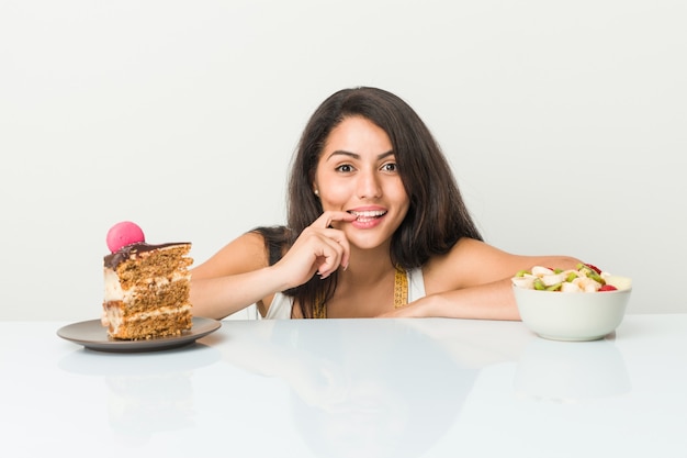 De jonge Spaanse vrouw die tussen cake of fruit kiezen ontspande het denken over iets bekijkend een exemplaar.