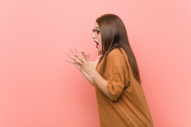 De jonge studentenvrouw die oogglazen draagt schreeuwt luid, houdt ogen geopend en handen gespannen.