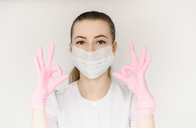 De jonge succesvolle arts in beschermend masker en witte laag toont teken met ok hand