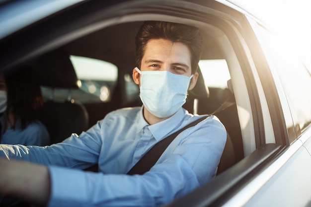 De jonge taxichauffeur van de jongen geeft passagier een rit die steriel medisch masker draagt.