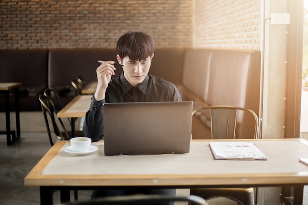 De jonge toevallige bedrijfsmens neemt een onderbreking en zit in de koffie en werkt aan zijn laptop