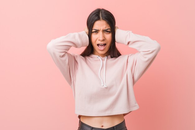 De jonge vrij Arabische vrouw die een toevallige sport draagt kijkt behandelend oren met handen die niet te hard geluid proberen te horen.