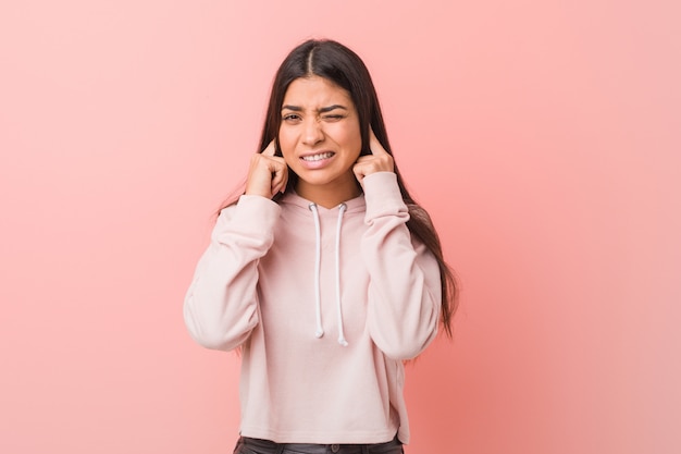 De jonge vrij Arabische vrouw die een toevallige sport draagt kijkt behandelend oren met handen.