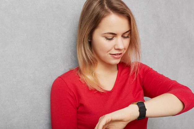 De jonge vrij jonge vrouw controleert tijd op polshorloge, die haast of laat voor vergadering is, wacht op iemand, vermoeid van wachten, geïsoleerd over grijze muur. Mensen, tijd, afspraak concept