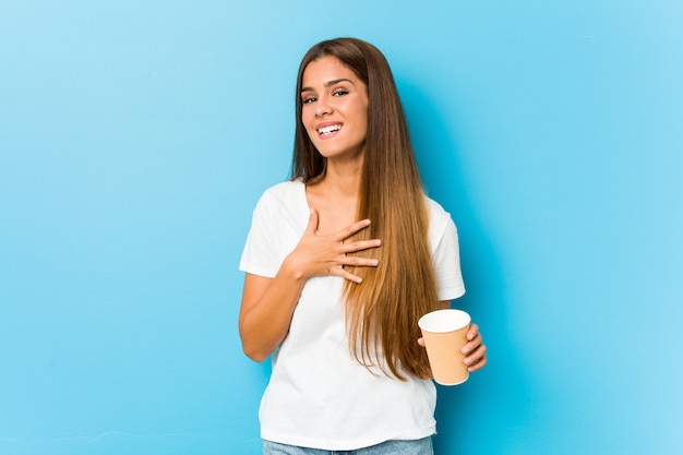 De jonge vrij Kaukasische vrouw die een meeneemkoffie houden lacht hardop hand houdend op borst.