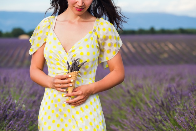 De jonge vrouw bevindt zich met lavendelbloemen in een holding van de wafelkop in een hand.