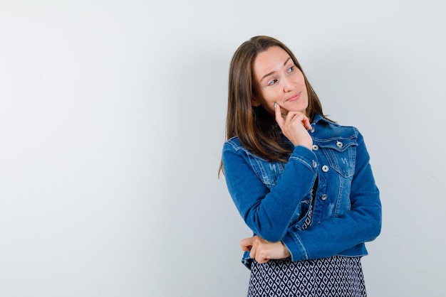 De jonge vrouw denkt door de wijsvinger op de wang op een witte achtergrond te leggen