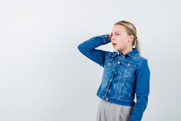 De jonge vrouw denkt door haar hand op het hoofd op een witte achtergrond te houden