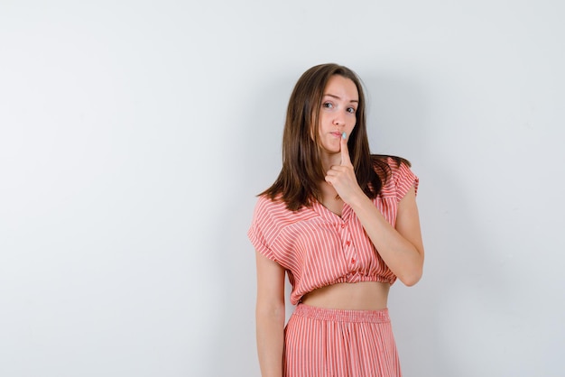 De jonge vrouw denkt door haar wijsvinger op de lippen op een witte achtergrond te leggen