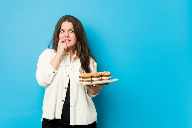 De jonge vrouw die cupcakes houden ontspande het denken over iets bekijkend een lege ruimte.