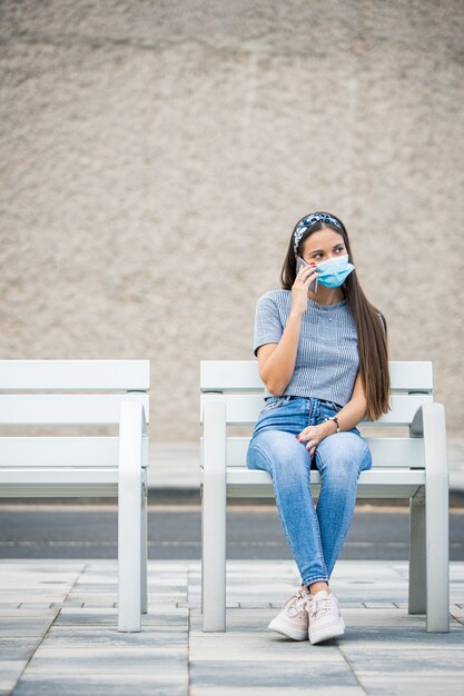 De jonge vrouw die een gezichtsmasker draagt, spreekt aan de telefoon