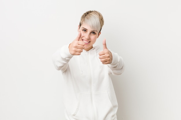 De jonge vrouw die een witte hoodie met duimen UPS draagt, juicht over iets toe