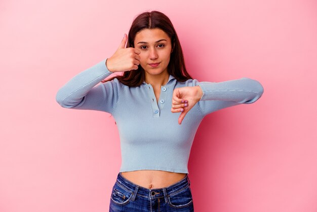 De jonge vrouw die op roze muur wordt geïsoleerd die duimen omhoog en duimen omlaag toont, moeilijk kiest concept