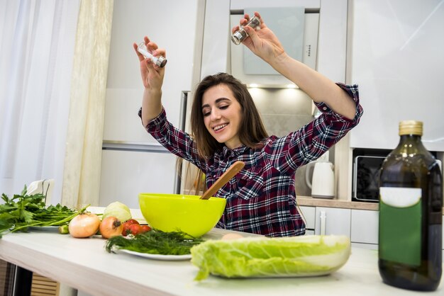 Foto de jonge vrouw die salade met groenten voorbereidt, voegt zout en peper toe voor betere smaak.