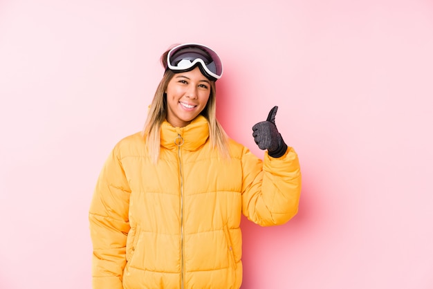 De jonge vrouw die skikleding draagt in een roze die en duim glimlachen opheffen omhoog
