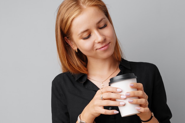 De jonge vrouw die van Nice een kop van koffie over een grijze achtergrond houdt