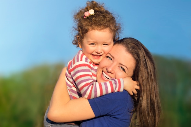 De jonge vrouw heeft pret, glimlacht met haar leuk kindbabymeisje. Portret van moeder, klein kind dochter buitenshuis op zonnige zomerdag. Moederdag, liefde, geluk, familie, ouderschap, concept kindertijd