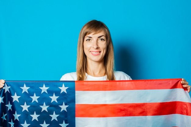 De jonge vrouw houdt de vlag van de VS voor haar op een blauwe achtergrond.