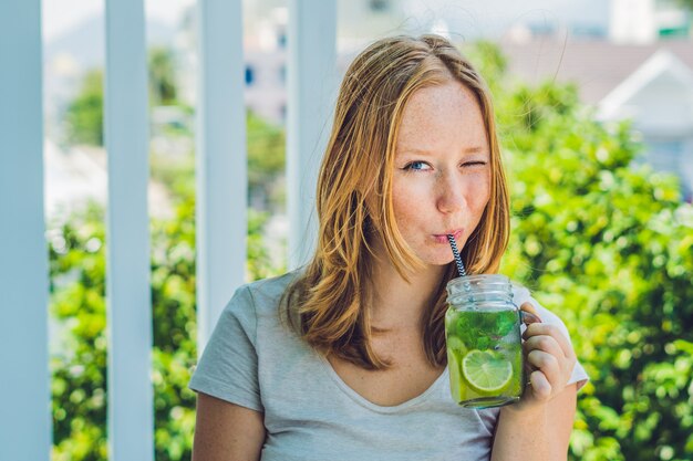 Foto de jonge vrouw houdt een metselaarkruik in haar hand met een mojito