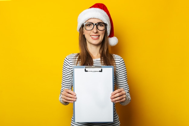 De jonge vrouw in een hoed van de Kerstman houdt een leeg klembord