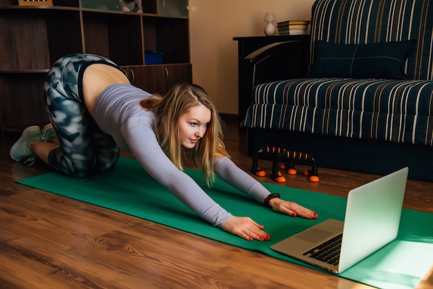 De jonge vrouw in yoga stelt thuis lettend op online klasse