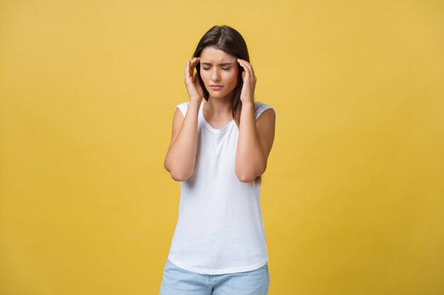 De jonge vrouw lijdt aan een hoofdpijn tegen een gele achtergrond.