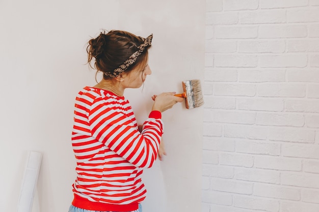 De jonge vrouw lijmt thuis behang. meisje lijmt behang in de vorm van een baksteen. reparatie.