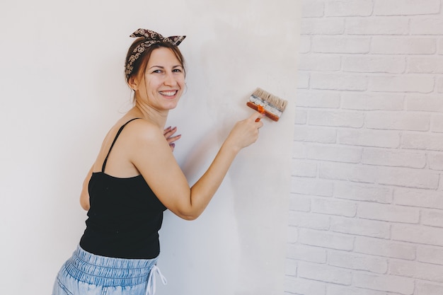 De jonge vrouw lijmt thuis behang. meisje lijmt behang in de vorm van een baksteen. reparatie.