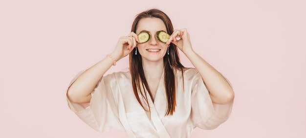 De jonge vrouw maakt het zelfgemaakte masker van de gezichtsschoonheid met plakjes komkommer