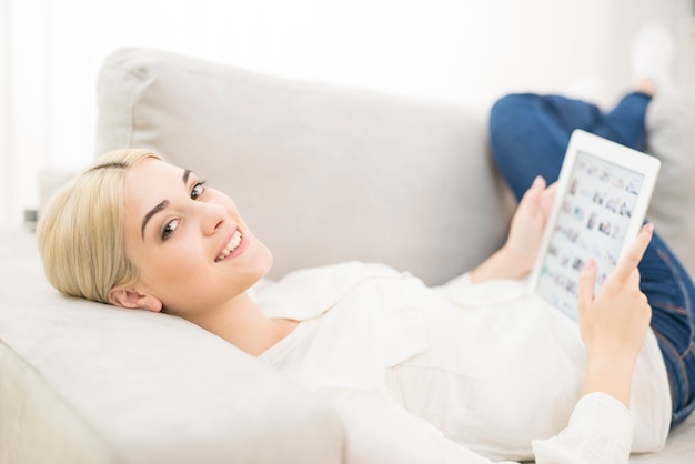 De jonge vrouw met een tablet lag op de bank