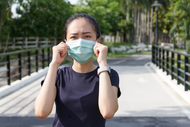 De jonge vrouw met medisch beschermend masker ontspannen in het park. campagne om een beschermend masker te gebruiken tegen COVID19