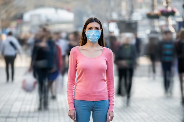 De jonge vrouw met medisch masker op haar gezicht staat op de drukke straat