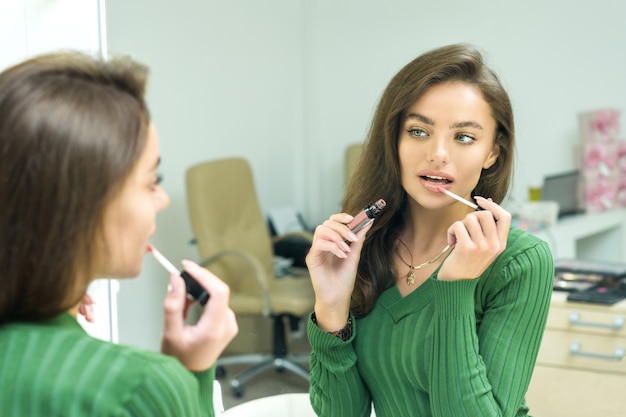 De jonge vrouw schildert lippen in beige