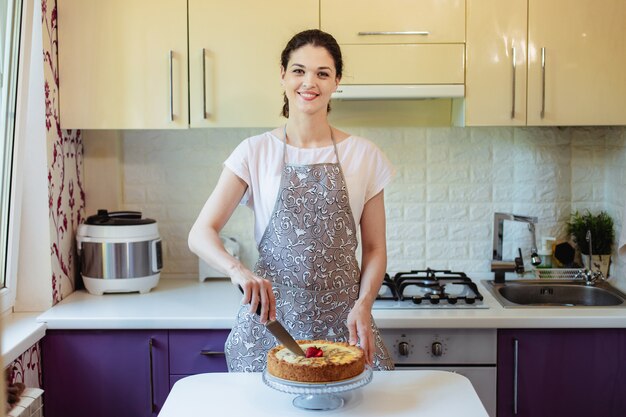 De jonge vrouw snijdt een pastei in de keuken