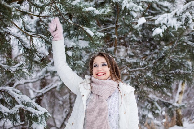 De jonge vrouw trekt een sparrentak en gooit sneeuw op zichzelf De vrouw gekleed in warme kleren heeft plezier in het winterpark