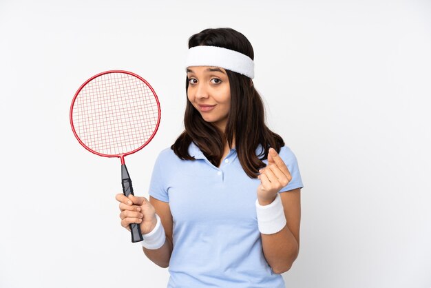 De jonge vrouw van de badmintonspeler over geïsoleerde witte achtergrond die geldgebaar maakt