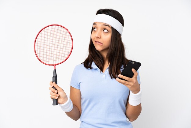 De jonge vrouw van de badmintonspeler over wit die koffie houdt om mee te nemen en een mobiel terwijl hij iets denkt