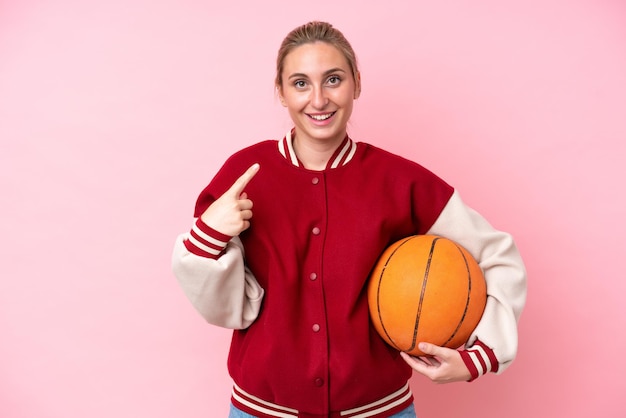 De jonge vrouw van de basketbal kaukasische speler die op roze achtergrond wordt geïsoleerd die een duim omhoog gebaar geeft