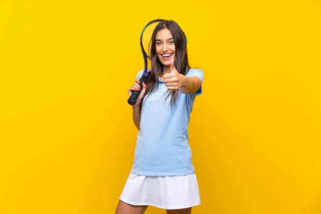 De jonge vrouw van de tennisspeler over geïsoleerde gele muur met omhoog duimen omdat er iets goeds is gebeurd
