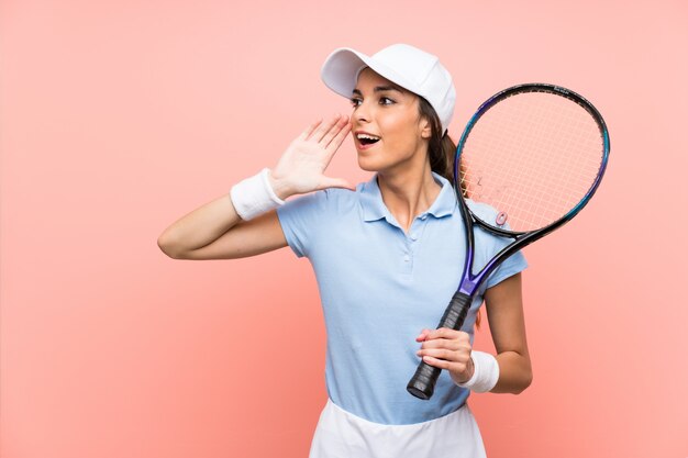 De jonge vrouw van de tennisspeler over geïsoleerde roze muur die met wijd open mond schreeuwen