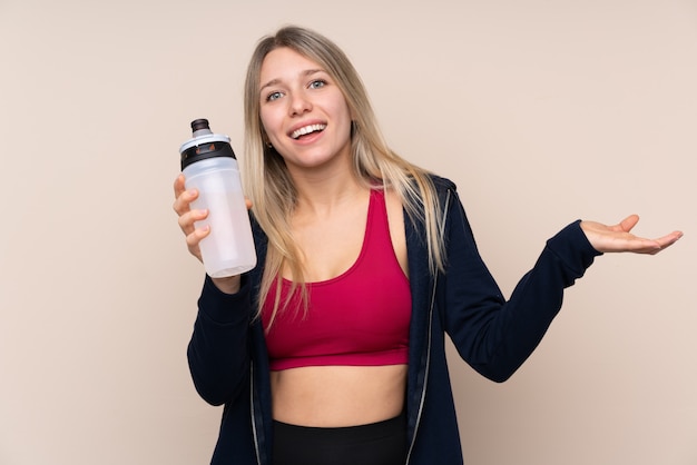 De jonge vrouw van het sportblonde over geïsoleerde muur met de fles van het sportenwater