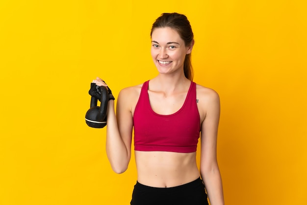 De jonge vrouw van Ierland die op gele achtergrond wordt geïsoleerd die Gewichtheffen met kettlebell maakt