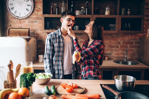 De jonge vrouw voedt echtgenoot een banaan op de keuken tijdens het koken van ontbijt.