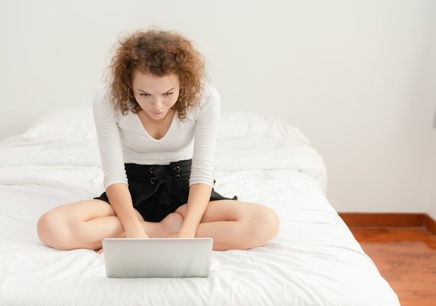 De jonge vrouw wekte terwijl het zoeken in haar laptop op bed in de ochtend op