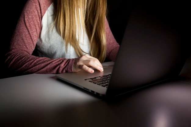 De jonge vrouw zitten in de donkere woonkamer en werken met laptop