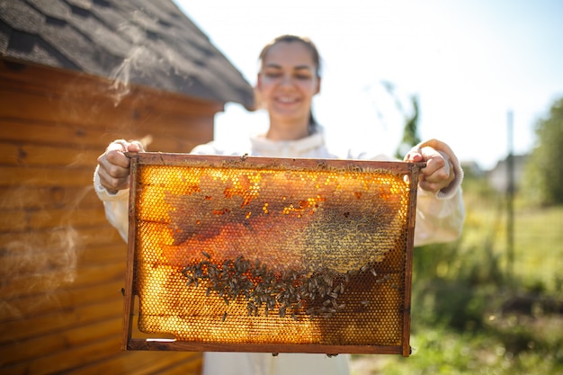 Foto de jonge vrouwelijke imker houdt houten kader met honingraat.