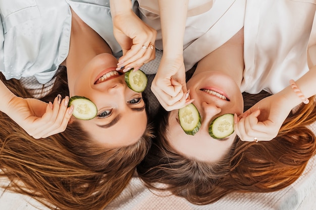 De jonge vrouwen maken het zelfgemaakte masker van de gezichtsschoonheid met plakjes komkommer