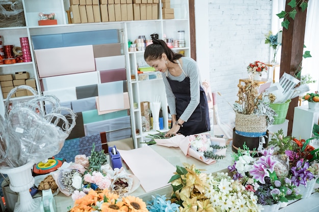 De jonge vrouwenbloemist die in bloemenwinkel werkt, maakt ordeflanelbloem in een lijstwerkruimte