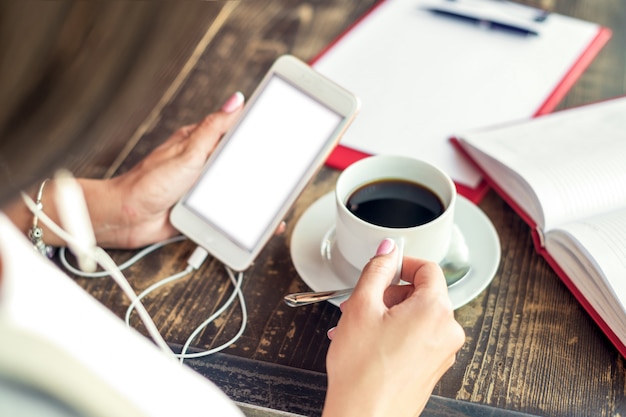 De jonge vrouwenhand gebruikt het telefoon witte scherm bij koffie openlucht.