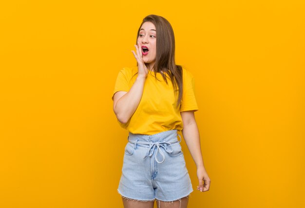 De jonge vrouwentiener die een geel overhemd draagt, zegt een geheim heet remmend nieuws en kijkt opzij